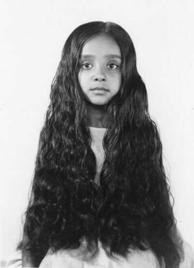 Black and white photograph of a seated girl with long black wavy hair covering her upper body